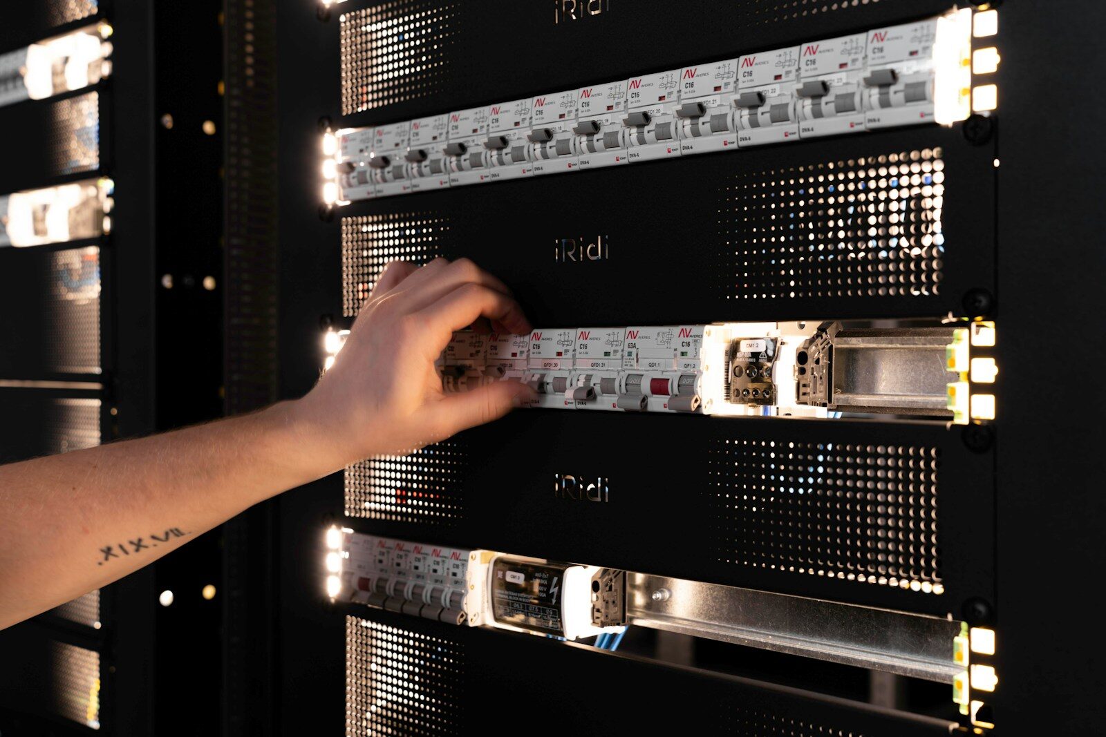 A hand adjusting components in a glowing server rack.
