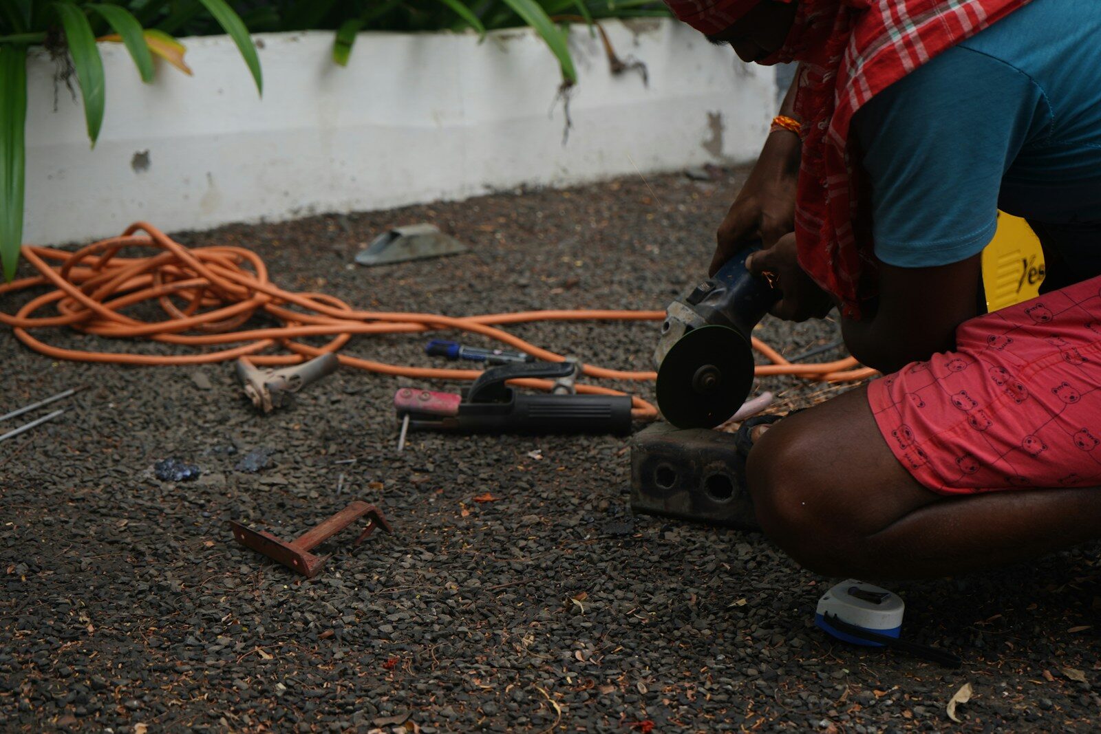 A person using an angle grinder on a metal block on gravel ground.